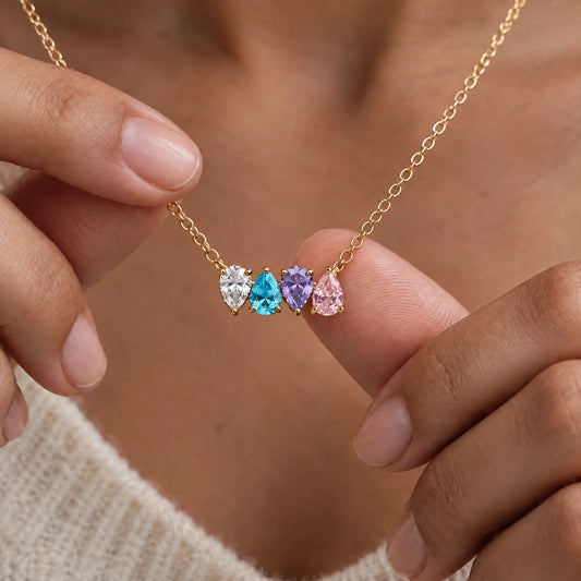 Collar Raíces en oro con cuatro piedras de nacimiento, sostenido entre dos dedos
