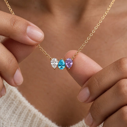 Collar Raíces en oro con tres piedras de nacimiento, sostenido entre dos dedos